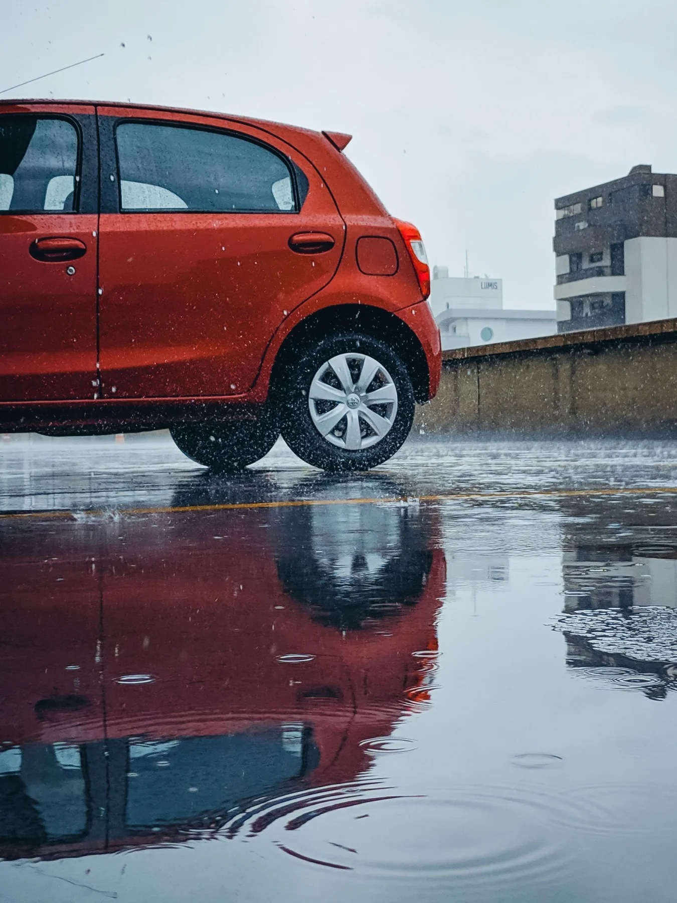Red hatchback and its reflection on rain-soaked ground